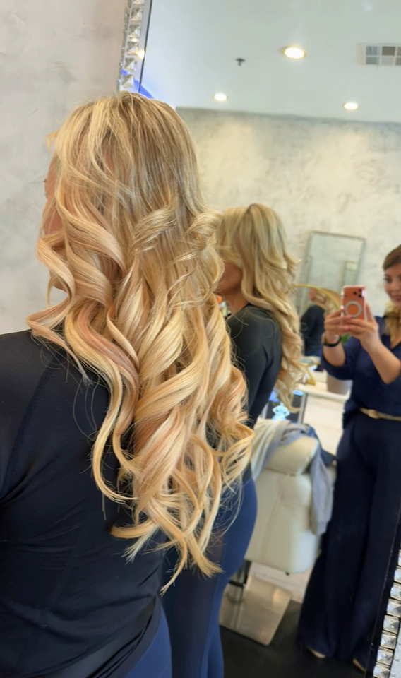 Long blonde hair styled in soft curls at Roza Glam